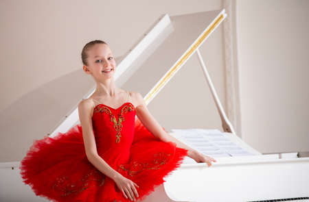 cute little girl dreams of becoming professional ballerina. In a white room, he stands at the piano in bright red pack. Vocational school student.の写真素材