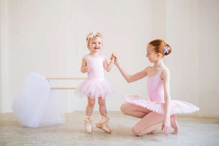 older sister, a ballerina in a pink tutu and pointe shoes, shows the baby how to practice at barre.の写真素材