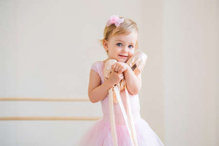 Portrait of cute blue-eyed baby ballerina in pink hugging pointe shoes.の写真素材