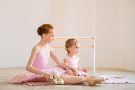 older sister, a ballerina in a pink tutu and pointe shoes, shows the baby how to practice at barre.の写真素材