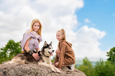 Siberian Husky and his family are sitting on a rock against the sky. The concept of love for animals and nature.の写真素材