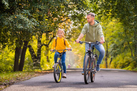 Happy father and daughter ride bicycles in the autumn park on a sunny day.の写真素材