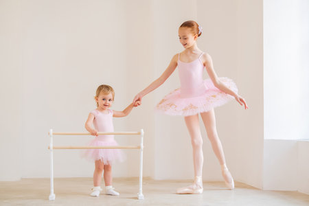 older sister, a ballerina in a pink tutu and pointe shoes, shows the baby how to practice at barre.の写真素材
