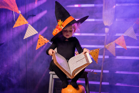 Happy Halloween. Cute cheerful little witch with a magic wand and book of spells conjures.の写真素材
