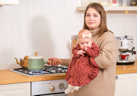Mother with a child in her arms cooks food in saucepan on the stoveの写真素材