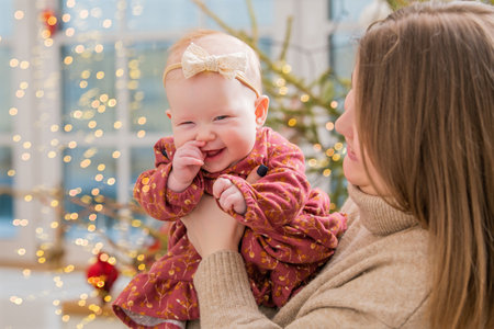 happy mother plays with a baby in her arms at home not against the background of a decorated room and a Christmas tree.の写真素材