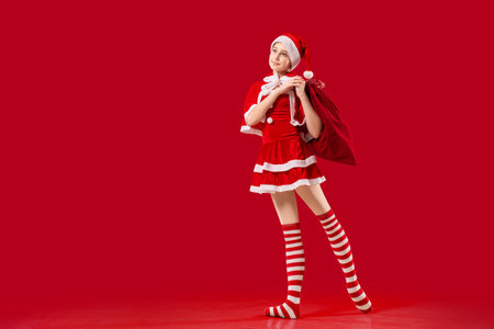 Dancing ballerina girl in pointe shoes with gift in her hands dressed as Santa Claus on red background.の写真素材