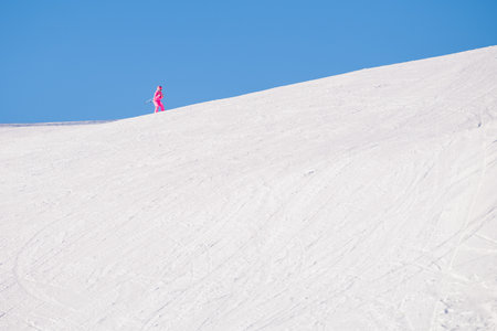 Happy person in red jacket skiing down slope in bright sunshine on blue sky, with high snow covered mountains in background. Blurred motion.の写真素材