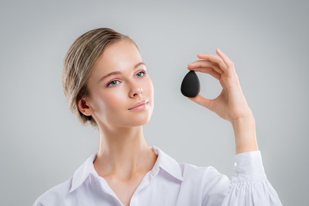 Cute beautiful natural brunette girl cleaning face with cotton sponge smiling looking at camera over white background. Cosmetology and spa.の写真素材