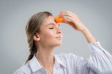 Cute beautiful natural brunette girl cleaning face with cotton sponge smiling looking at camera over white background. Cosmetology and spa.の写真素材