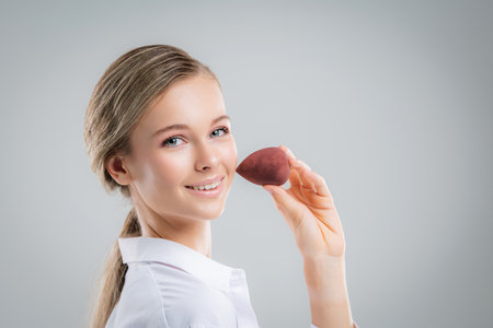 Cute beautiful natural brunette girl cleaning face with cotton sponge smiling looking at camera over white background. Cosmetology and spa.の写真素材