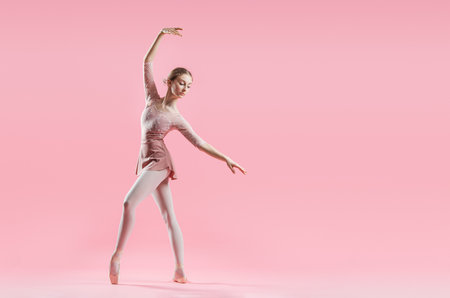 elegant young ballerina in pointe shoes dancing on a delicate pink backgroundの写真素材