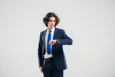 portrait of a handsome young man in dark blue business suit looking at his watch on a white background.の写真素材