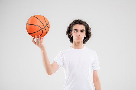 Smiling teenager, basketball player posing with ball in his hand on white background.の写真素材