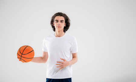 Smiling teenager, basketball player posing with ball in his hand on white background.の写真素材