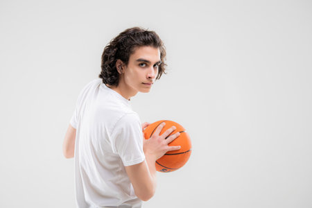 Smiling teenager, basketball player posing with ball in his hand on white background.の写真素材