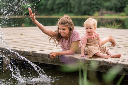 Portrait of two sisters children playing near the water onbackground of the lake and the forest. The concept of happy childhood, happy family.の写真素材