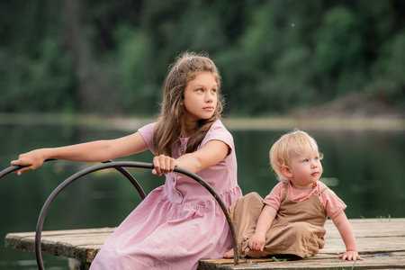 Portrait of two sisters children playing near the water onbackground of the lake and the forest. The concept of happy childhood, happy family.の写真素材