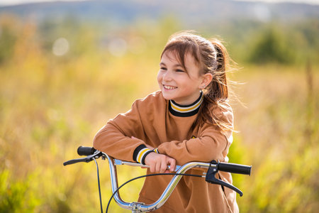 beautiful schoolgirl girl rides a scooter in an autumn park on sunny day.の写真素材