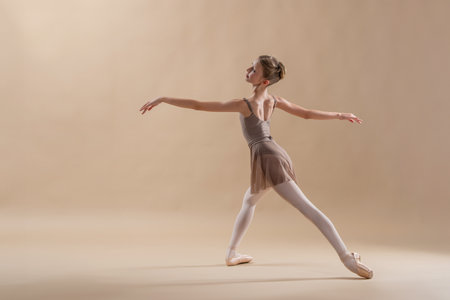 Beautiful young girl professional student ballerina in pointe shoes and a leotard on light beige background.の写真素材