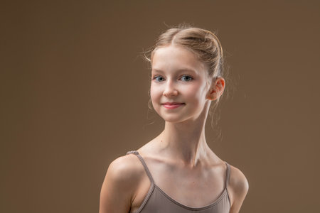 Portrait of beautiful young girl professional ballerina student with pointe shoes in a leotard on a light beige background.の写真素材