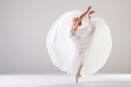 young ballerina in pointe shoes dances in long flying white skirt on a white backgroundの写真素材