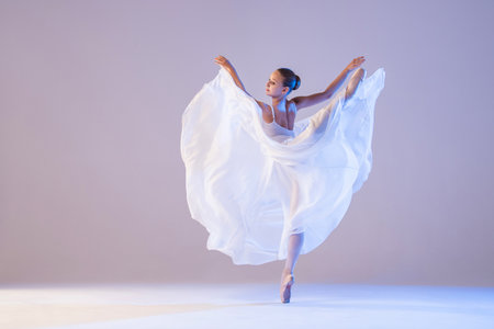 young ballerina in pointe shoes dances in long flying white skirt on a white backgroundの写真素材