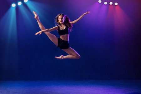 Beautiful young performer of modern choreography dancing in the spotlights on a black background.の写真素材