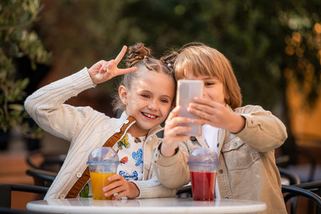 Teenage children chat happily together, take selfies and drink a fruit cocktail while sitting at a...