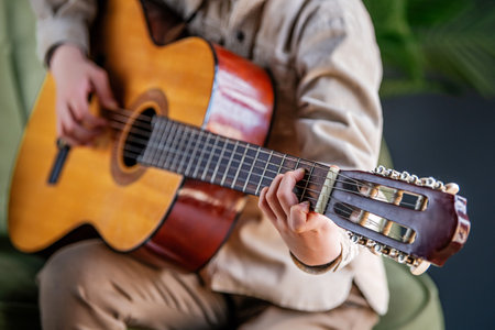 A person is playing a guitar. The guitar is brown and has a black head. The person is sitting on a...