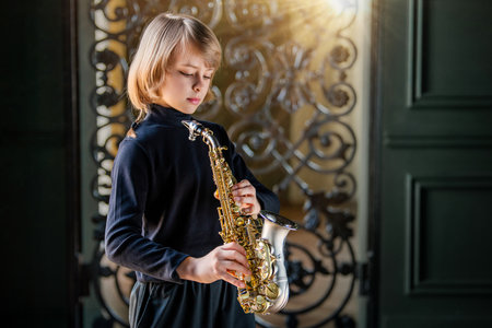 A young boy is playing a saxophone in front of a wrought iron gate. Concept of creativity and passion for music, as the girl is fully engaged in her performanceの写真素材