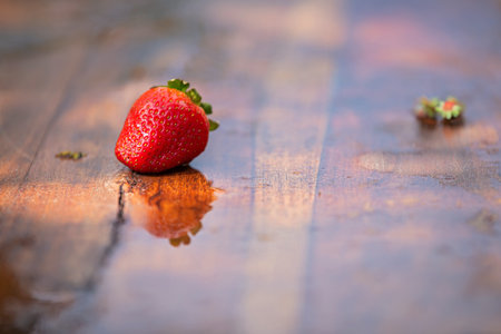 A red strawberry is sitting on a wooden table. The reflection of the strawberry can be seen in the waterの写真素材