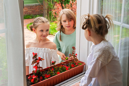 Children communicate through the open window of a country house. The window sill is decorated with a box of red flowers.の写真素材