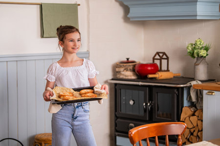 happy girl holding a baking tray with freshly baked pies in her hands in the interior of a country house kitchen.の写真素材
