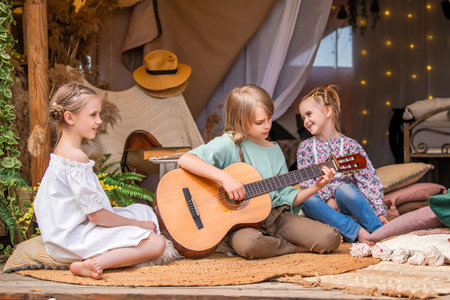 A tourist group of children relaxes and plays the guitar in a tent. Active children's recreation in nature. Learning to play the guitar.の写真素材