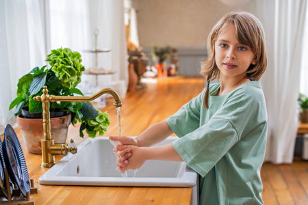 a child washes his hands under a brass faucet in the interior of a country house kitchen.の写真素材