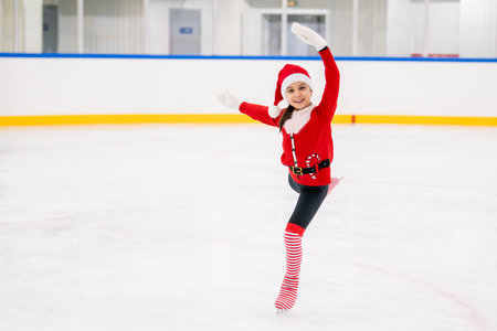 Little girl figure skater dressed as Santa Claus skates on the ice of the indoor arena. Christmas holiday for athletes.の写真素材