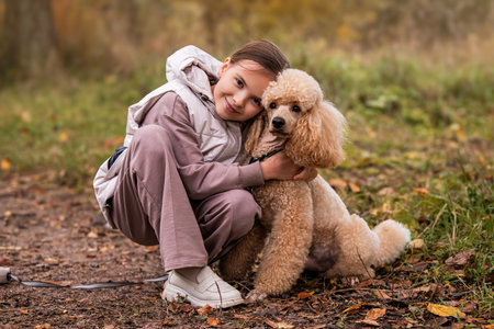 Adorable little girl hugging her poodle dog on a walk in the autumn park.の写真素材