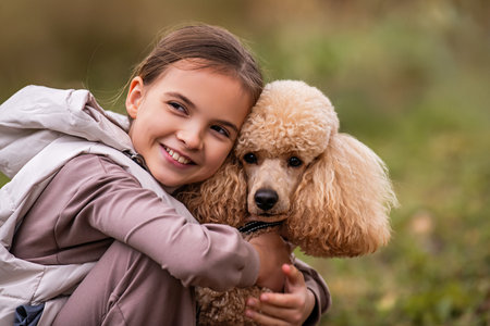 Adorable little girl hugging her poodle dog on a walk in the autumn park.の写真素材