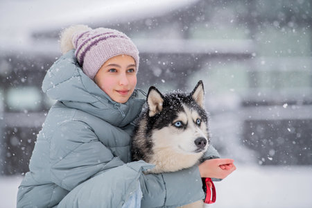 Young woman walking her Siberian Husky dog in the snow on a winter day, training and walking her dog. Friendship, dog on a walk with its ownerの写真素材