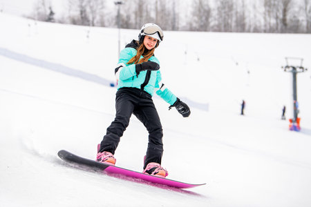 Young female snowboarder gliding down a snowy slope, dressed in stylish winter gear. Exciting winter sports and outdoor adventure.の写真素材