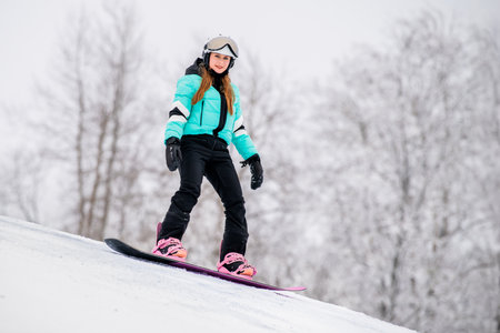 Young female snowboarder gliding down a snowy slope, dressed in stylish winter gear. Exciting winter sports and outdoor adventure.の写真素材