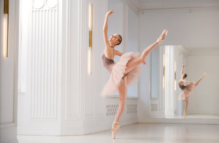 ballerina in a beige leotard and tutu gracefully poses on pointe in a bright ballet studio, her reflection in the mirror completing the scene.の写真素材