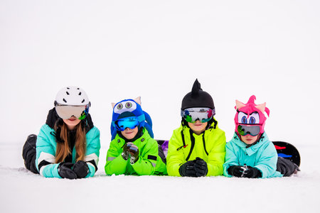 group of children and teenagers lie in the snow at a ski resort. Ski lifts and skiers are visible in the background. The atmosphere is cheerful and carefree, emphasizing the joy of winter recreation.の写真素材