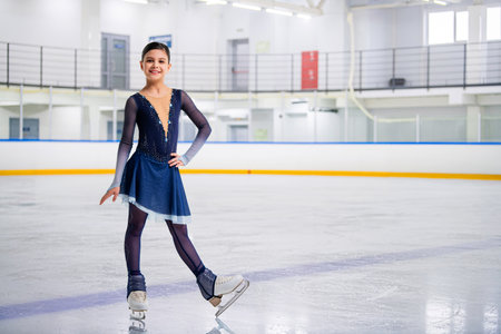 A young girl is skating on ice with a smile on her face. She is wearing a black outfit and is wearing glovesの写真素材