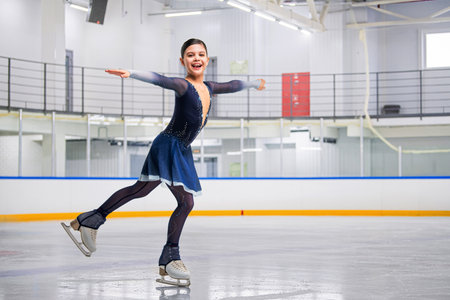 young girl figure skater is skating on ice with a smile on her face. She is wearing a blue outfit dress and is wearing glovesの写真素材