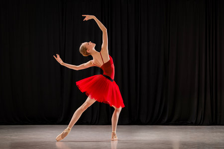 A young ballerina in a red tutu with a fan performs a variation from the ballet on the theater stage.の写真素材