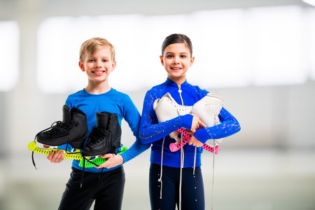 A pair of young figure skaters, a boy and a girl, in a bright costume holding skates - preparing for ice training.の写真素材