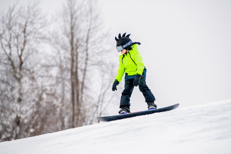 Young snowboarder in bright neon jacket riding downhill on snowy slope. Exciting winter sports and outdoor adventure.の写真素材