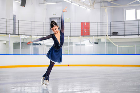 young girl figure skater is skating on ice with a smile on her face. She is wearing a blue outfit dress and is wearing glovesの写真素材